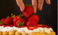 Mão retirando um morango de um monte deles num bolo com creme branco para usar comida no sexo.
